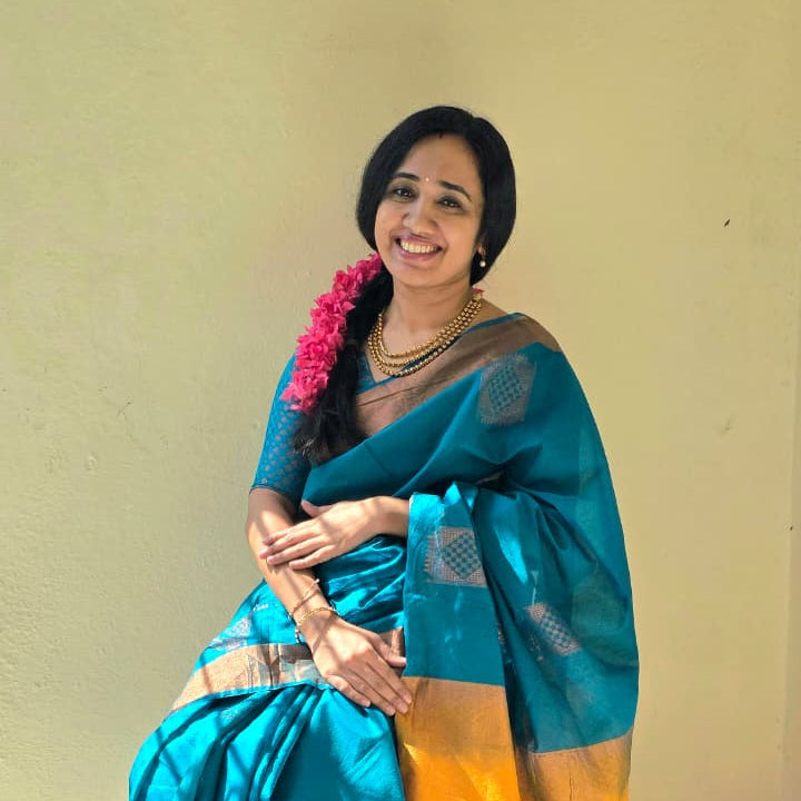 Woman in a blue saree with gold border against a beige wall
